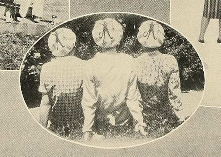 Three girls sitting side by side, wearing berets with devils on them.